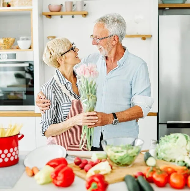 An elderly couple happily preparing food together in their kitchen. They are surrounded by fresh ingredients, conveying a sense of joy, connection, and healthy living. The image supports the idea that dietary improvements can be a shared and enjoyable activity that enhances cognitive function, as highlighted in 'New Study Reveals: The Link Between Diet and Cognitive Function in Older Adults'.