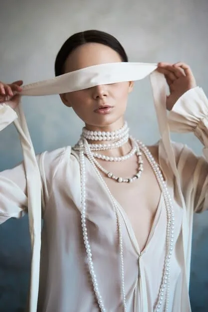 A woman wearing a silk scarf tied in a necklace knot, positioned at the center of her chest, with the ends cascading down her blouse. The focus is on the detailed knot and how it complements her outfit.