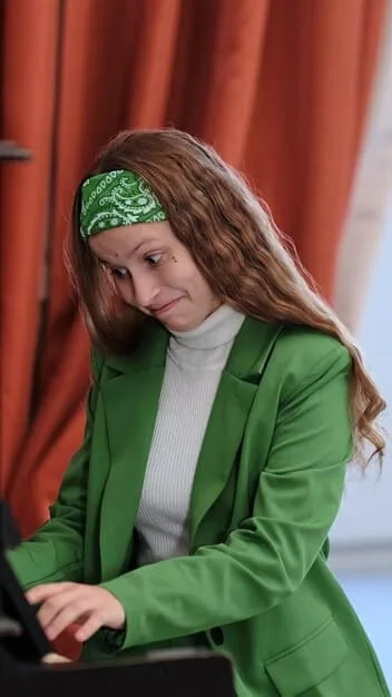 A professional woman in a modern office wearing a well-tailored emerald green blazer over a neutral top, signifying strong presence. Her hands are gently clasped, and her expression is confident but approachable.