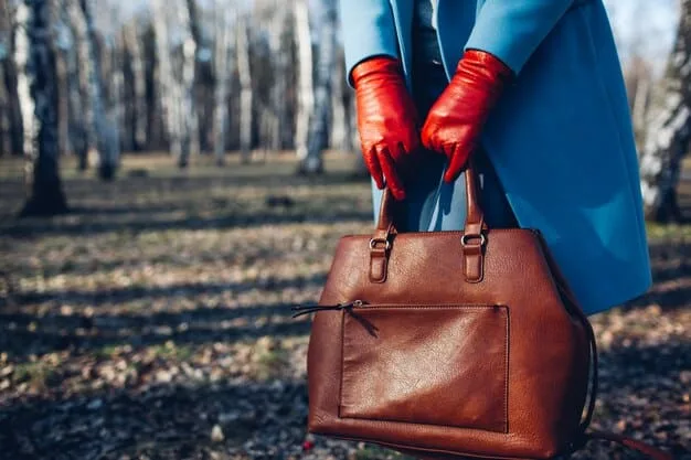 A close-up of a woman tying a vibrant silk scarf around the handle of her classic leather handbag, showing how accessories can instantly refresh an existing item.