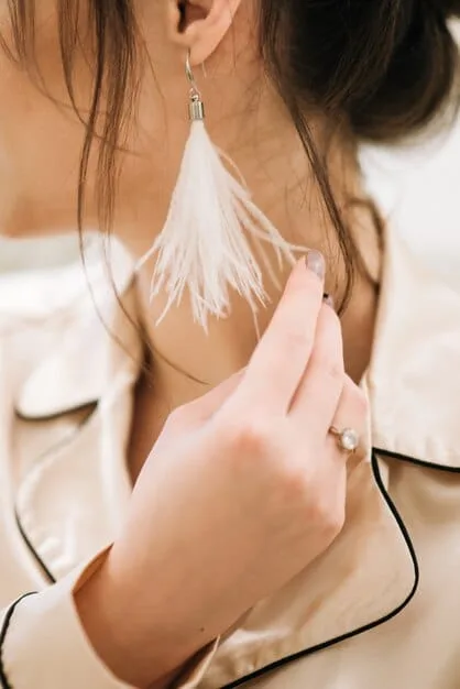 A close-up shot of a hand gently adjusting a delicate silver hoop earring, with soft focus on the ear and a blurred background of a neatly styled closet, emphasizing the everyday elegance of simple jewelry.