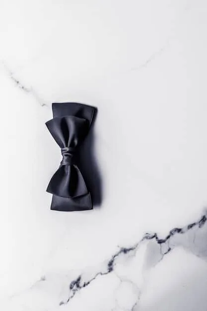 A detailed close-up of a perfectly tied black bow tie on a crisp white shirt, symbolizing formal attire, with a soft-focus background of elegant event decor.