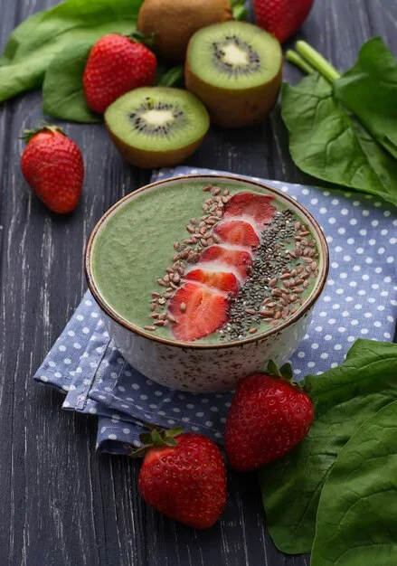 A vibrant, colorful smoothie bowl filled with fresh berries, spinach, and nuts, with a small glass of water beside it, signifying healthy nutrition and hydration.