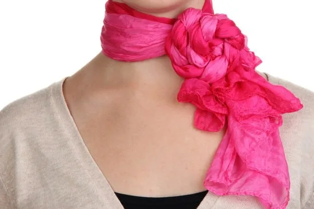 A close-up of a woman's neck, showcasing a neatly tied silk scarf with a vibrant floral pattern. The scarf is styled in a