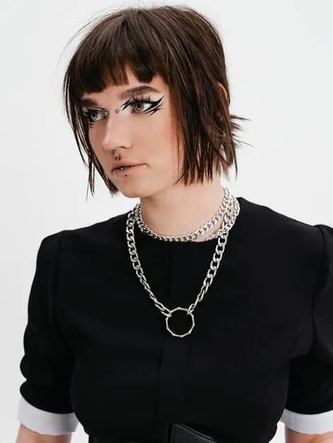 A woman with a chic bob haircut wearing an elegant silver chain necklace with a small pendant, complementing her classic-style dress with a V-neckline, showcasing how the necklace frames her face and enhances her attire.