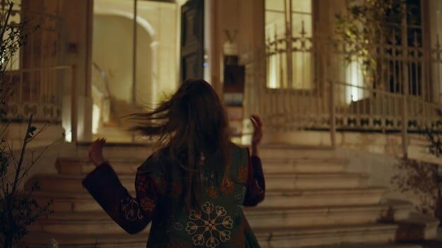 A woman elegantly dressed, walking through a softly lit corridor, with a subtle fragrance aura effect emanating from her.