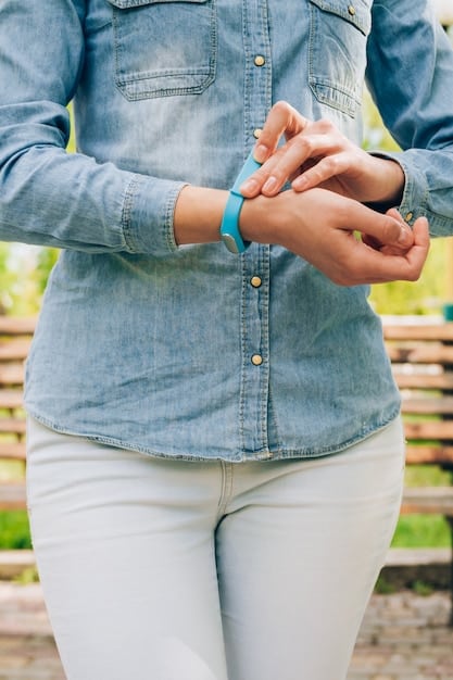 A person's wrist with three different blotter strips labeled with specific fragrance names. The hand is positioned near the nose, indicating the act of smelling the fragrances thoughtfully. The background is blurred, emphasizing the focus on the fragrance samples.