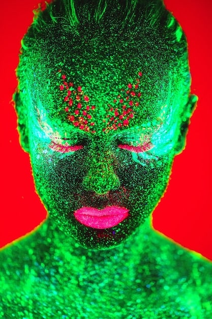 A person with bright neon green eyeshadow extending outwards in a cat-eye shape, heavily coated in chunky silver glitter, creating a bold, futuristic look.