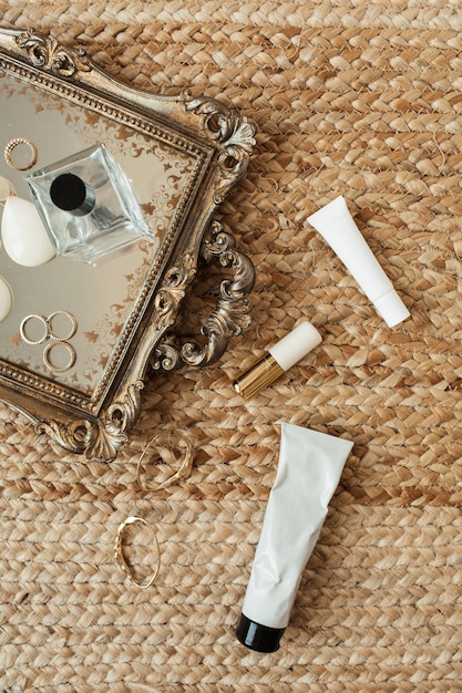 A selection of minimalist makeup products arranged on a vanity, including a tinted moisturizer, cream blush, clear brow gel, and a lip balm. The lighting is soft and natural, highlighting the textures of the products.