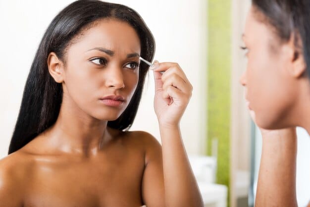 A close-up shot of a woman gently pinching her natural and false eyelashes together with an eyelash applicator, ensuring a seamless blend.