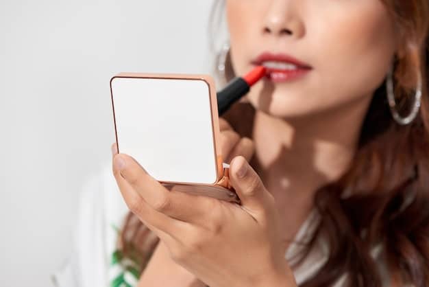A hand applying lipstick with a brush, carefully layering the product onto the lips. The background is a makeup vanity with various beauty products.