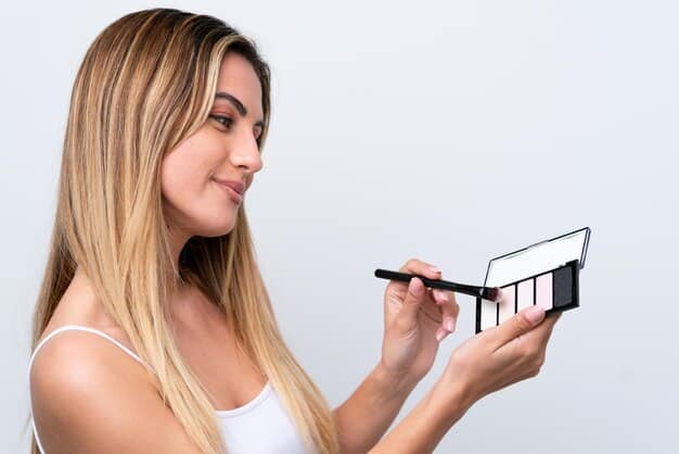 A woman holding up different styles of false eyelashes in front of her eye, comparing the length and volume of each style. The background is a well-lit vanity with various makeup products.