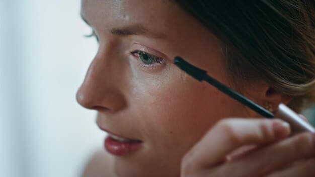 A woman applying eyeshadow primer to her eyelid with a small brush. The focus is on the texture of the primer and the smooth, even application.