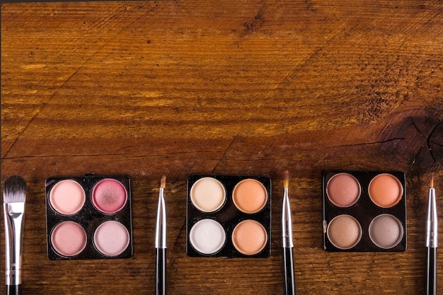A flat lay of various highlighter products including powder compacts, cream sticks, and liquid illuminators, arranged on a clean white background. The products range in shades from pearlescent white to champagne and rose gold.