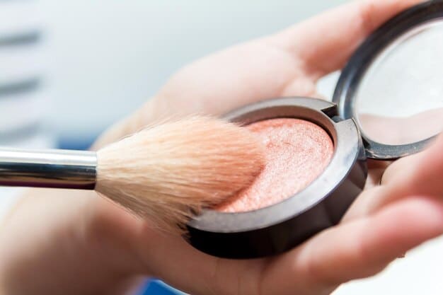 A close up of a makeup artists hand applying blush to a models cheek. The blush brush is soft and the color is a subtle pink.