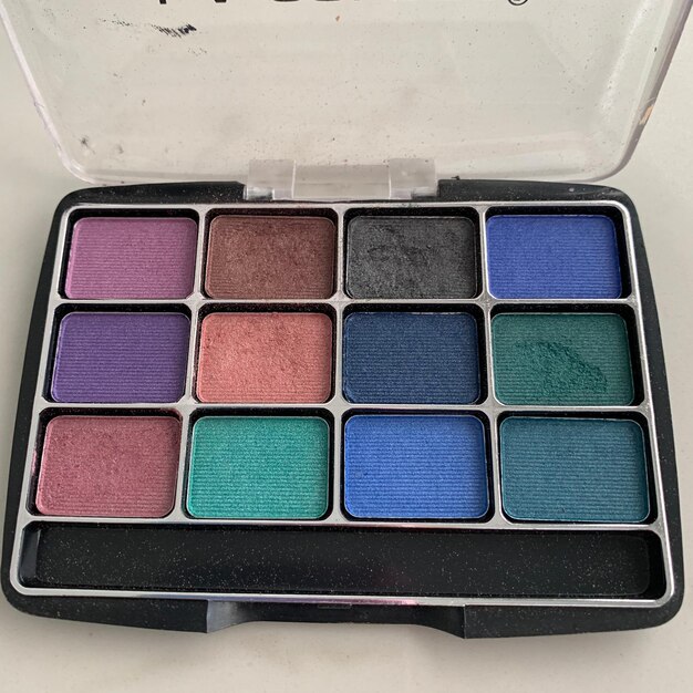 A makeup palette featuring cool-toned eyeshadows in shades of silver, ice blue, and deep plum, along with a shimmering highlighter and a dark berry lipstick.