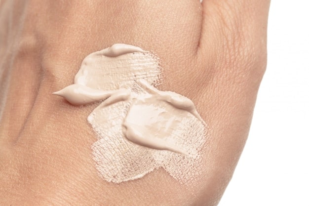 A hand applying tinted moisturizer to a clean face, with a focus on the natural skin texture and the even distribution of the product. Soft, natural lighting.