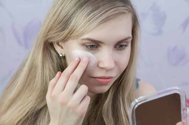 A woman applying a tinted moisturizer to her face with her fingertips, ensuring even coverage. She is in a brightly lit bathroom with a clean and minimalist aesthetic. The focus is on her hand and the product application.
