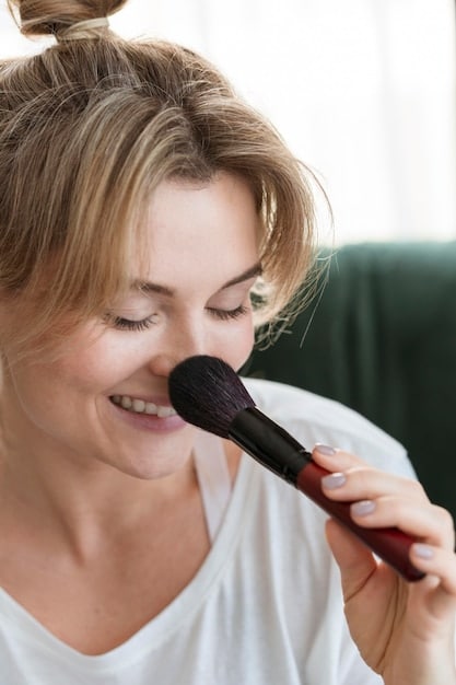 A woman applying mineral powder with SPF using a large, fluffy brush. The focus is on the powder and the brush as she gently sweeps it across her face.