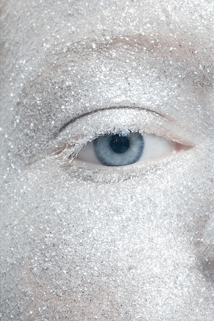 A close-up of a woman's eye with intricate icy blue and silver eyeshadow, delicate silver glitter accents, and perfectly applied mascara, highlighting the sparkle and depth of the winter wonderland eye makeup.