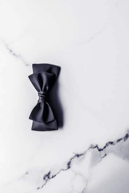A detailed close-up of a perfectly tied black bow tie on a crisp white shirt, symbolizing formal attire, with a soft-focus background of elegant event decor.