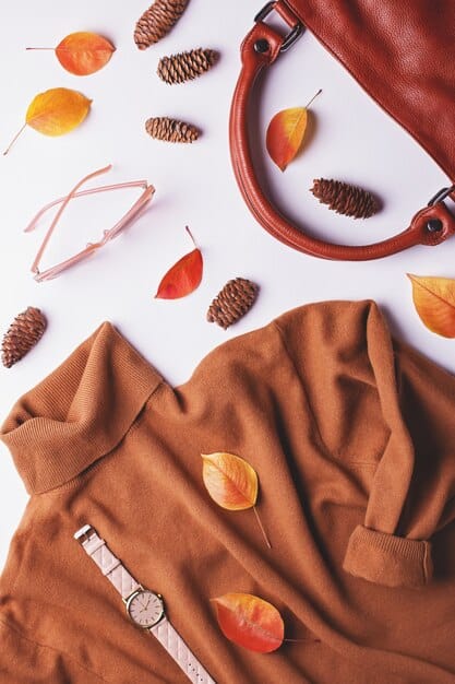 A flat lay of classic accessories, including a beige trench coat, a high-quality leather tote bag, minimalist gold jewelry, and a silk scarf, arranged neatly on a light-colored surface.