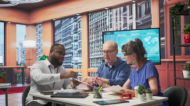 A diverse group of business professionals in a meeting, with charts displaying rising operational costs and healthcare expenses impacting their company's finances.