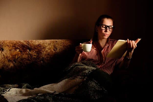 A person wearing orange-tinted blue light blocking glasses while reading a book in a dimly lit room with warm ambient lighting.