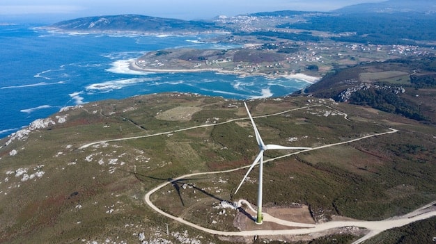 An aerial view of a large offshore wind farm in the Atlantic Ocean. The turbines are tall and white, contrasting against the blue sea. A small service vessel is visible navigating between the turbines. This symbolizes the growing importance of offshore wind in the 