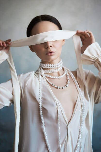 A woman wearing a silk scarf tied in a necklace knot, positioned at the center of her chest, with the ends cascading down her blouse. The focus is on the detailed knot and how it complements her outfit.