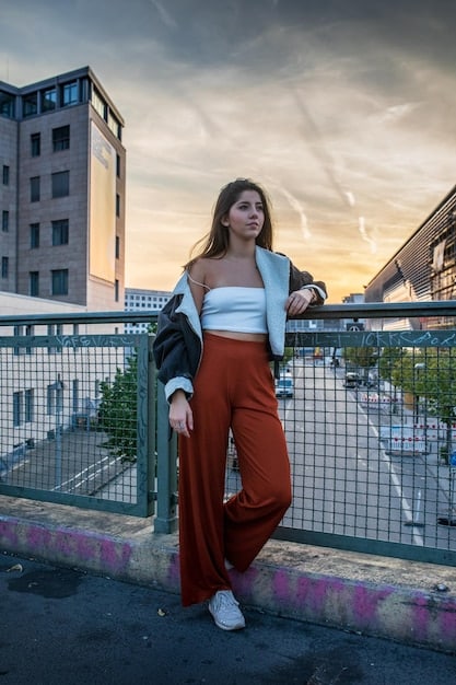 A young woman in her early 20s standing in a trendy urban setting; wearing high-waisted jeans, a crop top, and stylish sneakers.  She is holding a coffee cup and smiling confidently. The image showcases a relaxed but fashionable outfit, perfect for someone in their twenties, embodying How to Dress for Your Age: A Style Guide for Every Decade.