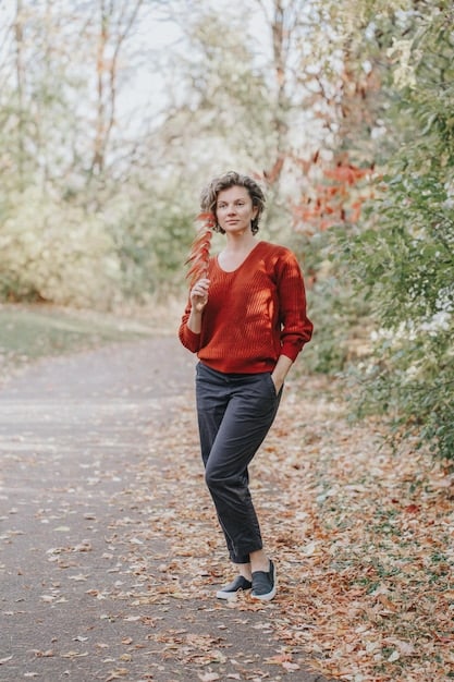 A woman in her 50s walking through a park; wearing a well-fitting trouser, cashmere sweater, and classic trench coat. She is wearing sunglasses, and carrying a stylish handbag. The image perfectly portrays How to Dress for Your Age: A Style Guide for Every Decade, demonstrating how to stay timeless and chic in your fifties.