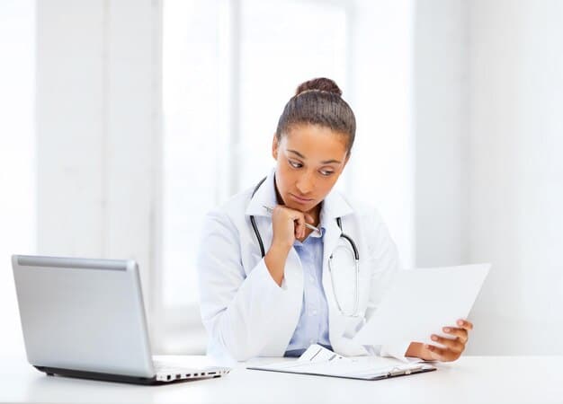 A person sitting at a desk, looking at a complex medical bill with a magnifying glass. The scene is well-lit and conveys a sense of careful review and scrutiny. The background includes a computer screen displaying healthcare-related information, reinforcing the context of navigating the US healthcare system.
