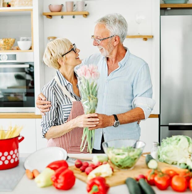 An elderly couple happily preparing food together in their kitchen. They are surrounded by fresh ingredients, conveying a sense of joy, connection, and healthy living. The image supports the idea that dietary improvements can be a shared and enjoyable activity that enhances cognitive function, as highlighted in 'New Study Reveals: The Link Between Diet and Cognitive Function in Older Adults'.